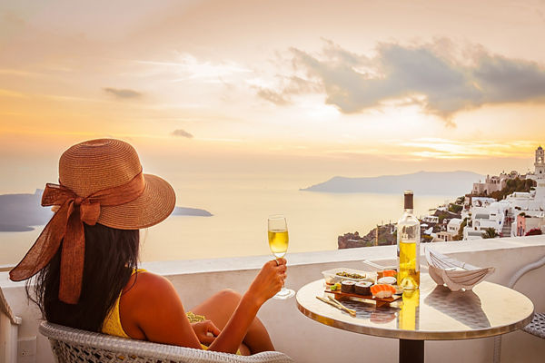 Female tourist enjoying food, wine and sunset view at Santorini, Greece